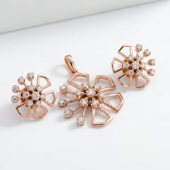 Elegant 18KT rose gold diamond floral pendant set featuring an open-petal flower design with a cluster of brilliant-cut diamonds at the center. The set includes a matching pendant and a pair of earrings, combining modern geometric petals with sparkling diamond accents for a contemporary floral look.