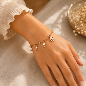 Elegant 18KT rose gold charm bracelet featuring delicate evil eye, fish, and Hamsa hand charms on a sleek link chain, beautifully worn on a woman's wrist, perfect for everyday wear, meaningful gifting, and symbolic protection.