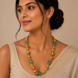 Woman wearing a 22K gold heritage necklace featuring carved emerald-green beads, intricate gold filigree beads, and oval kundan-inspired accents, paired with a beige saree for an elegant traditional look.
