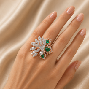 Luxurious gold statement ring featuring vivid green emerald-cut gemstones paired with clusters of marquise and baguette-cut diamonds in an intricate floral-inspired design.