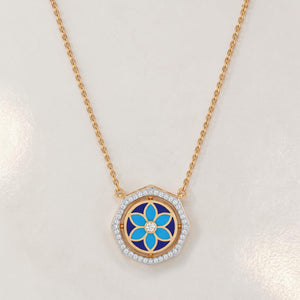 Elegant gold necklace featuring a hexagon-shaped pendant with blue floral enamel detailing and sparkling diamond accents on a white background.