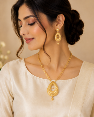 Elegant gold jewellery set featuring a detailed teardrop pendant necklace with intricate filigree work and matching ornate drop earrings, finished with delicate gold bead accents.