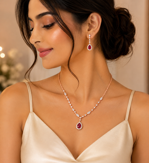 Elegant rose gold jewellery set featuring a delicate diamond-accented necklace with a pear-shaped ruby pendant and matching ruby drop earrings.