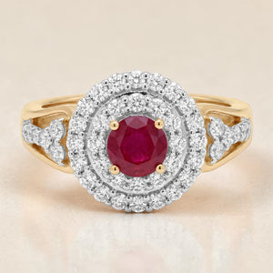 Yellow gold ring featuring a vibrant round ruby center stone secured with prongs, surrounded by a double halo of sparkling diamonds and diamond-accented shoulders for a classic luxurious look.