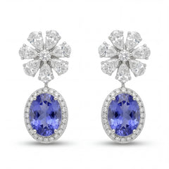 Elegant 18KT white gold drop earrings featuring oval blue tanzanite gemstones with diamond halo and floral diamond tops on a white background.
