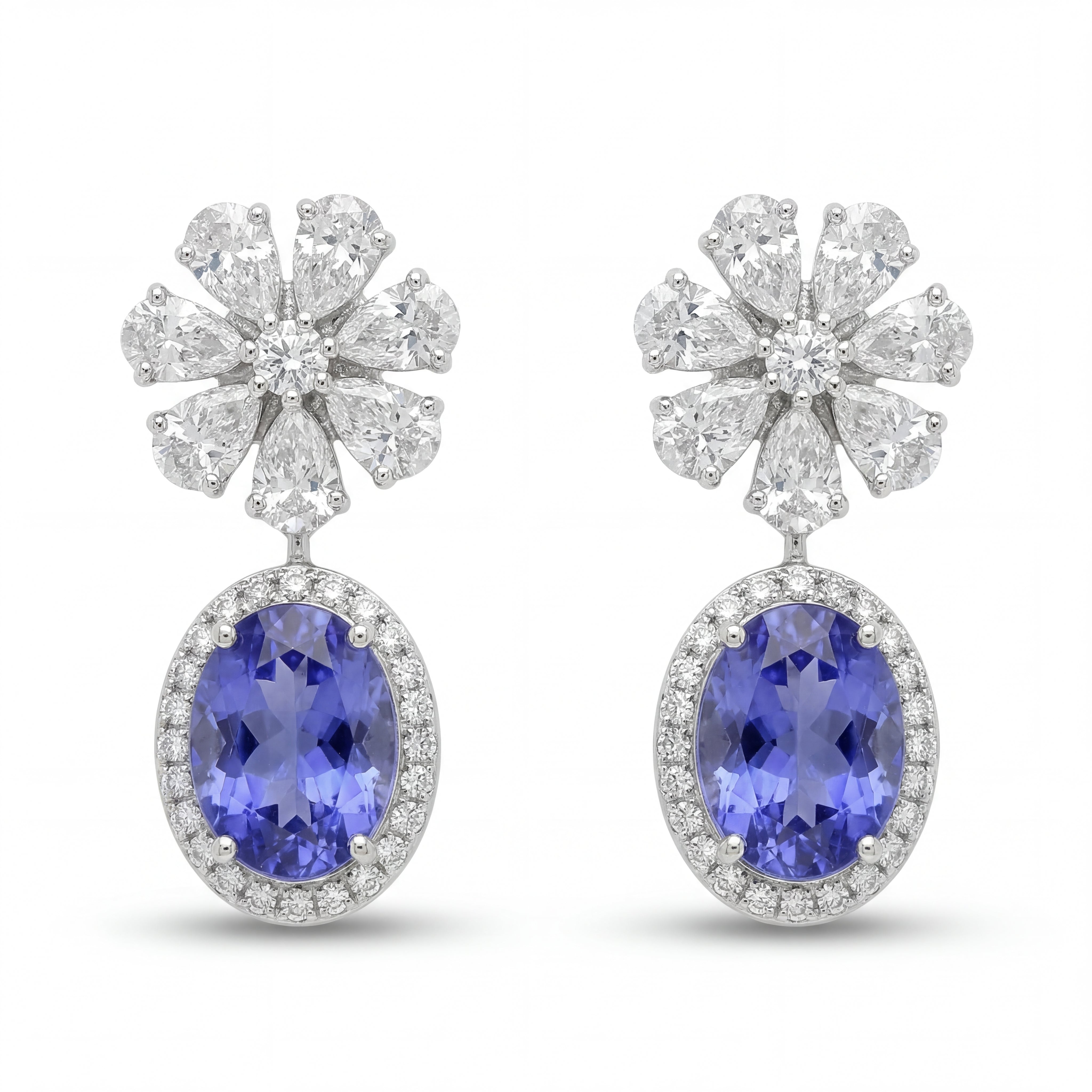 Elegant 18KT white gold drop earrings featuring oval blue tanzanite gemstones with diamond halo and floral diamond tops on a white background.