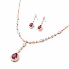 Elegant 18K rose gold necklace set featuring pear-shaped ruby drop pendant with diamond halo, marquise accents, and matching dangling ruby diamond earrings.
