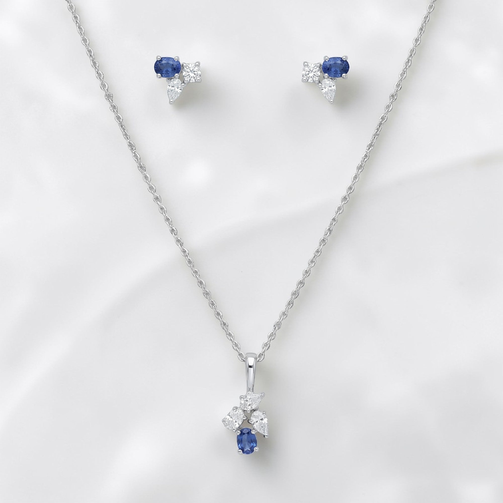 Luxurious 18K white gold sapphire diamond jewelry set featuring blue sapphire drop pendant with sparkling diamond cluster and matching earrings by Pachchigar Jewellers Ashokbhai