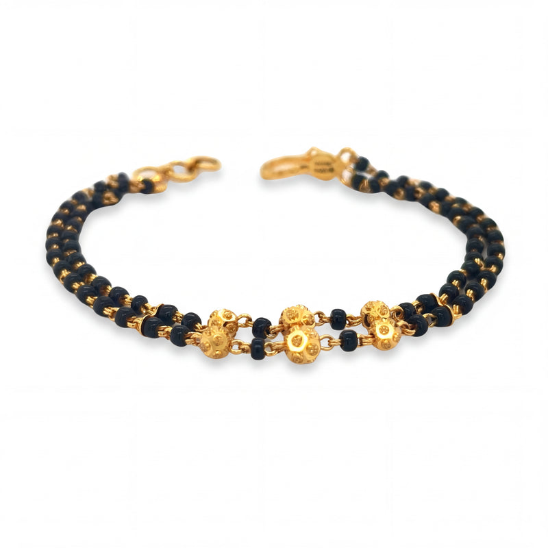 Elegant 22KT yellow gold bracelet featuring double-row black beads with floral gold centerpiece accents on a white background.