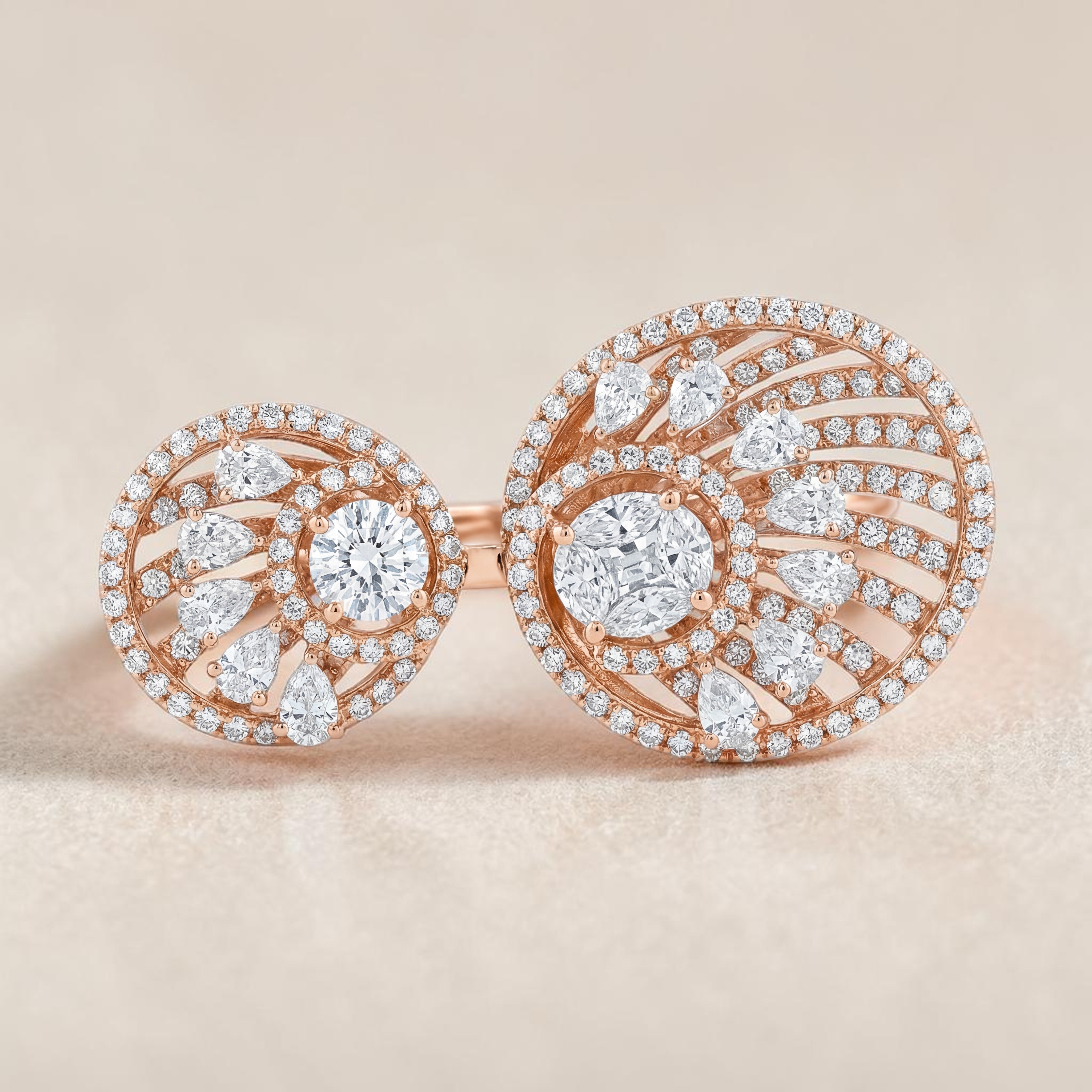 Modern open-style diamond ring in rose gold featuring two circular swirl motifs with a central round diamond, accented by pear-shaped and round diamonds in a spiral halo design.
