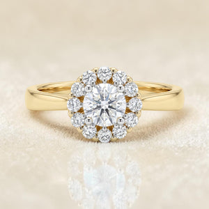 Yellow gold ring featuring a round brilliant solitaire diamond surrounded by a delicate halo of smaller diamonds, set on a sleek and minimal band for a timeless elegant look.