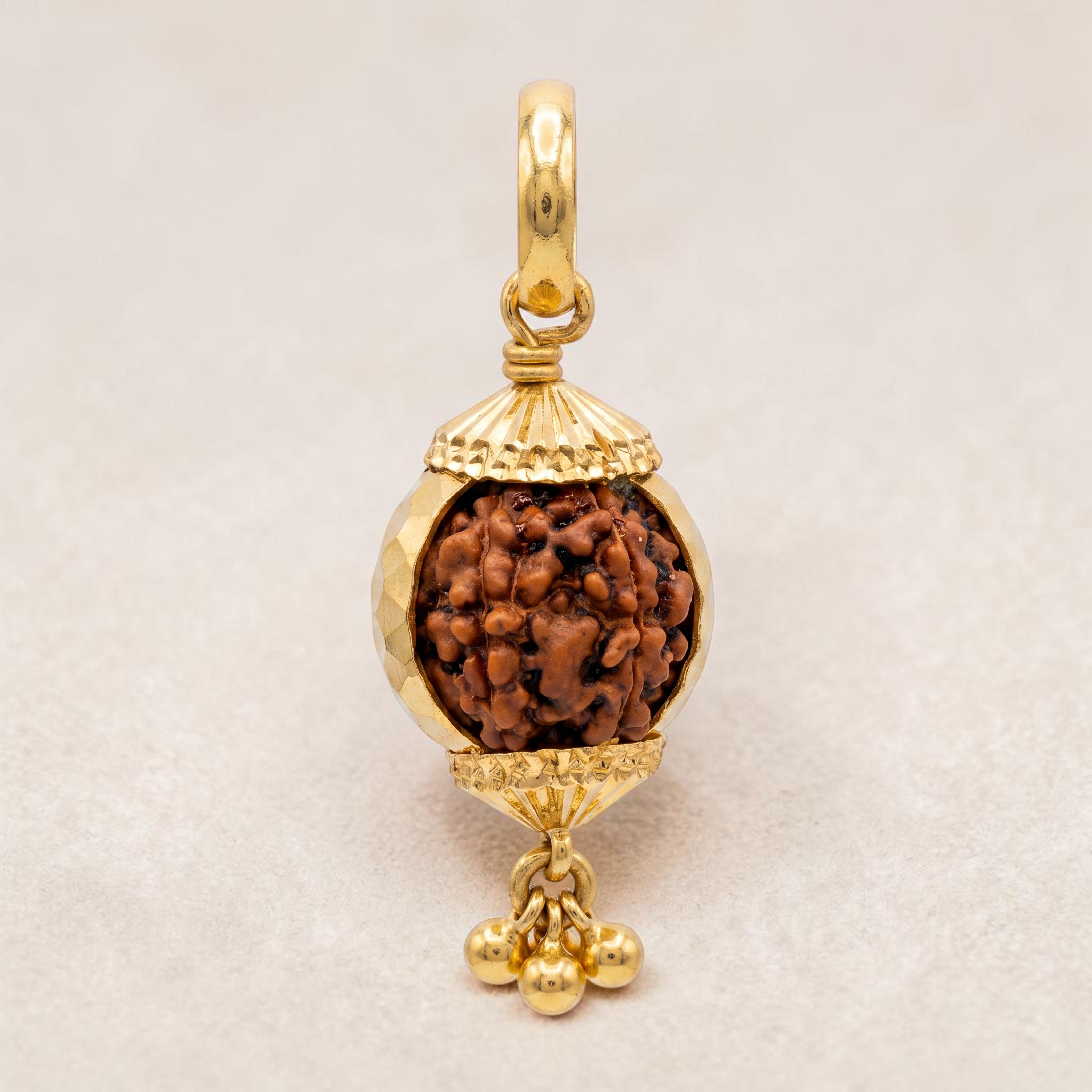 Yellow gold pendant featuring a spherical Rudraksha bead encased in a decorative gold frame with textured caps and small dangling gold beads, symbolizing spirituality and elegance.