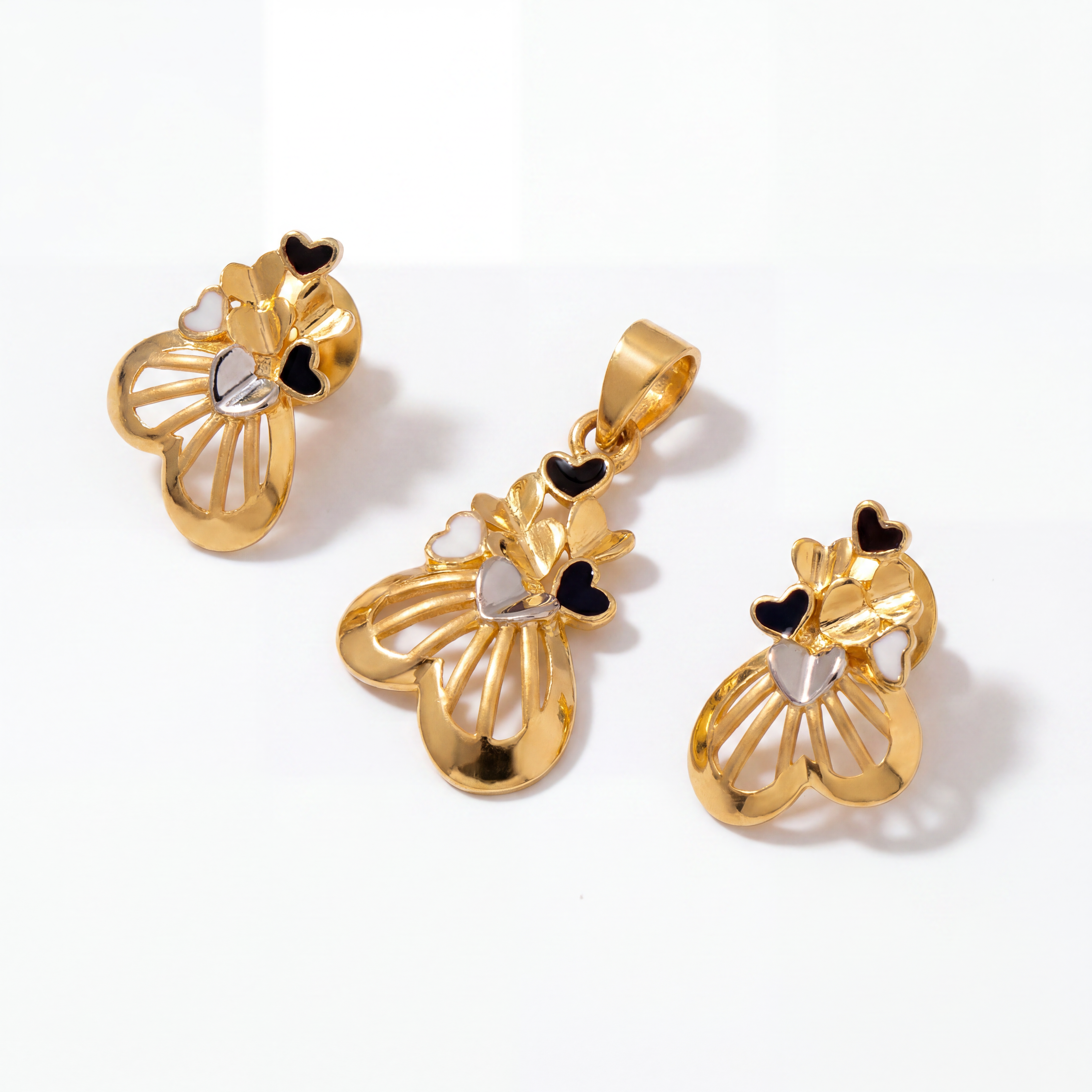 Elegant gold jewellery set featuring a heart-inspired pendant and matching earrings with black and white enamel detailing and intricate openwork design.