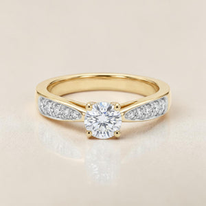 Yellow gold ring featuring a round brilliant solitaire diamond in a classic prong setting, with tapered shoulders accented by pavé-set diamonds for a refined and timeless design.