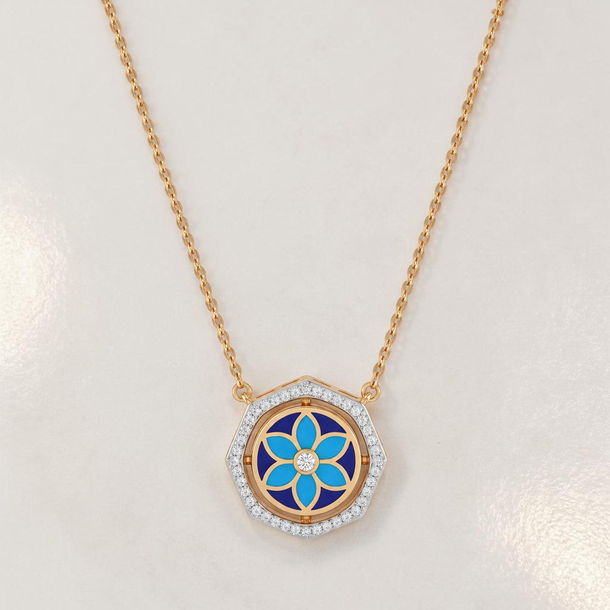 Elegant gold necklace featuring a hexagon-shaped pendant with blue floral enamel detailing and sparkling diamond accents on a white background.