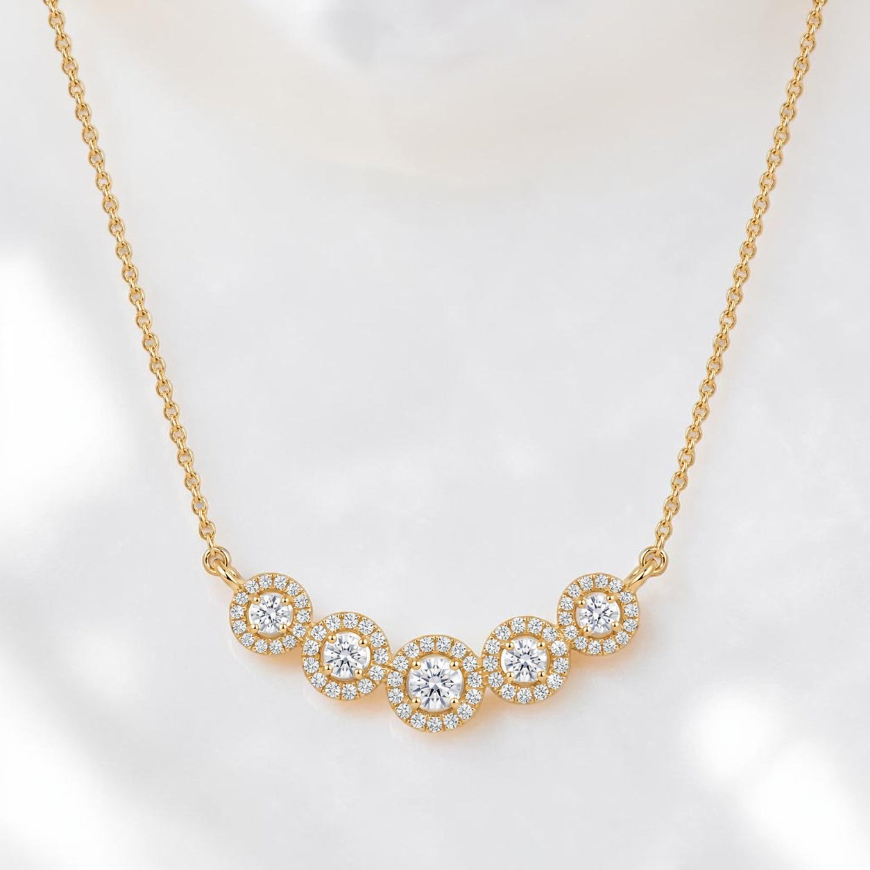 Elegant gold necklace featuring five sparkling round diamond halo motifs arranged in a graceful curved design on a white background.