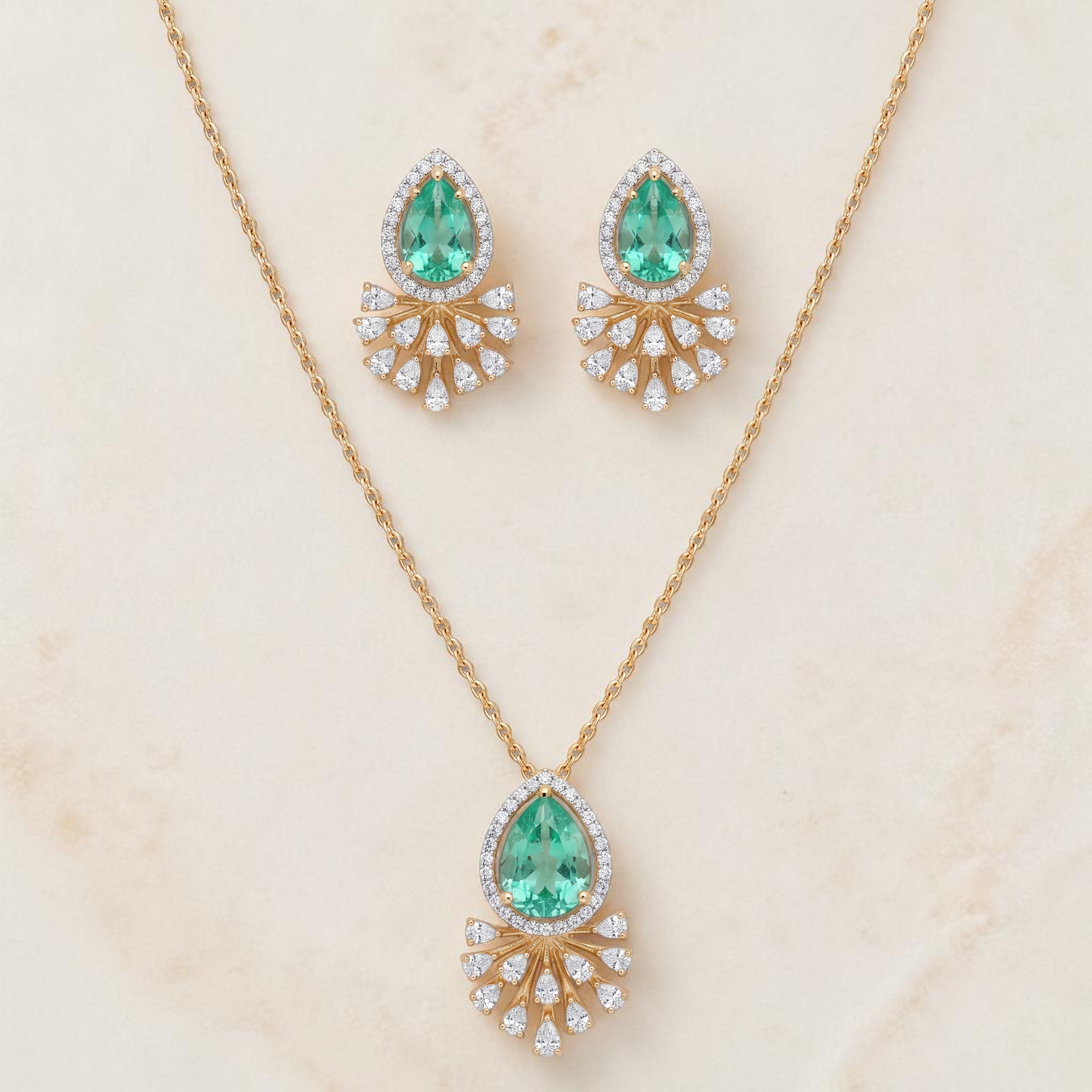Elegant gold jewelry set featuring teardrop-shaped emerald gemstones with sparkling diamond halo detailing in a pendant necklace and matching earrings on a white background.