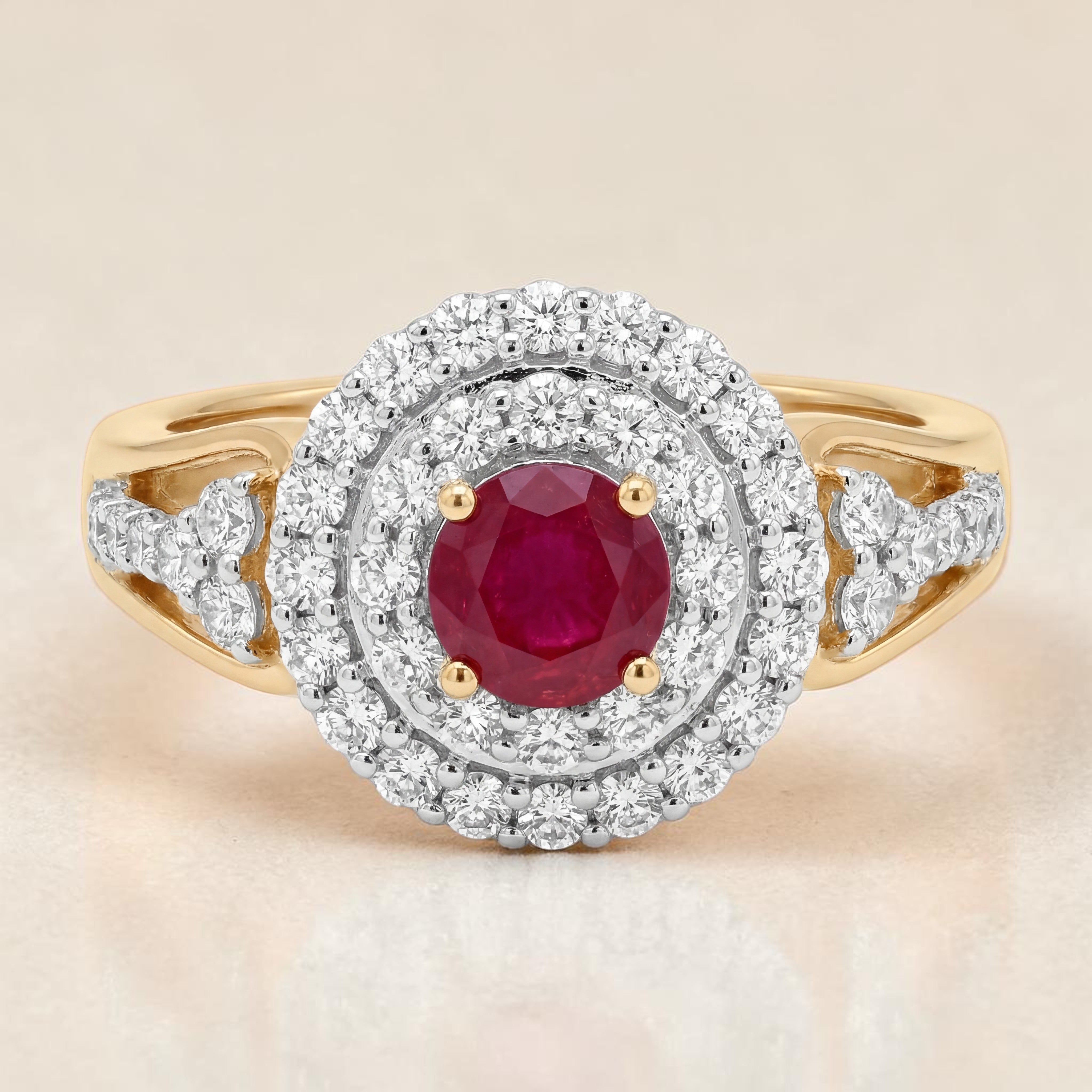 Yellow gold ring featuring a vibrant round ruby center stone secured with prongs, surrounded by a double halo of sparkling diamonds and diamond-accented shoulders for a classic luxurious look.