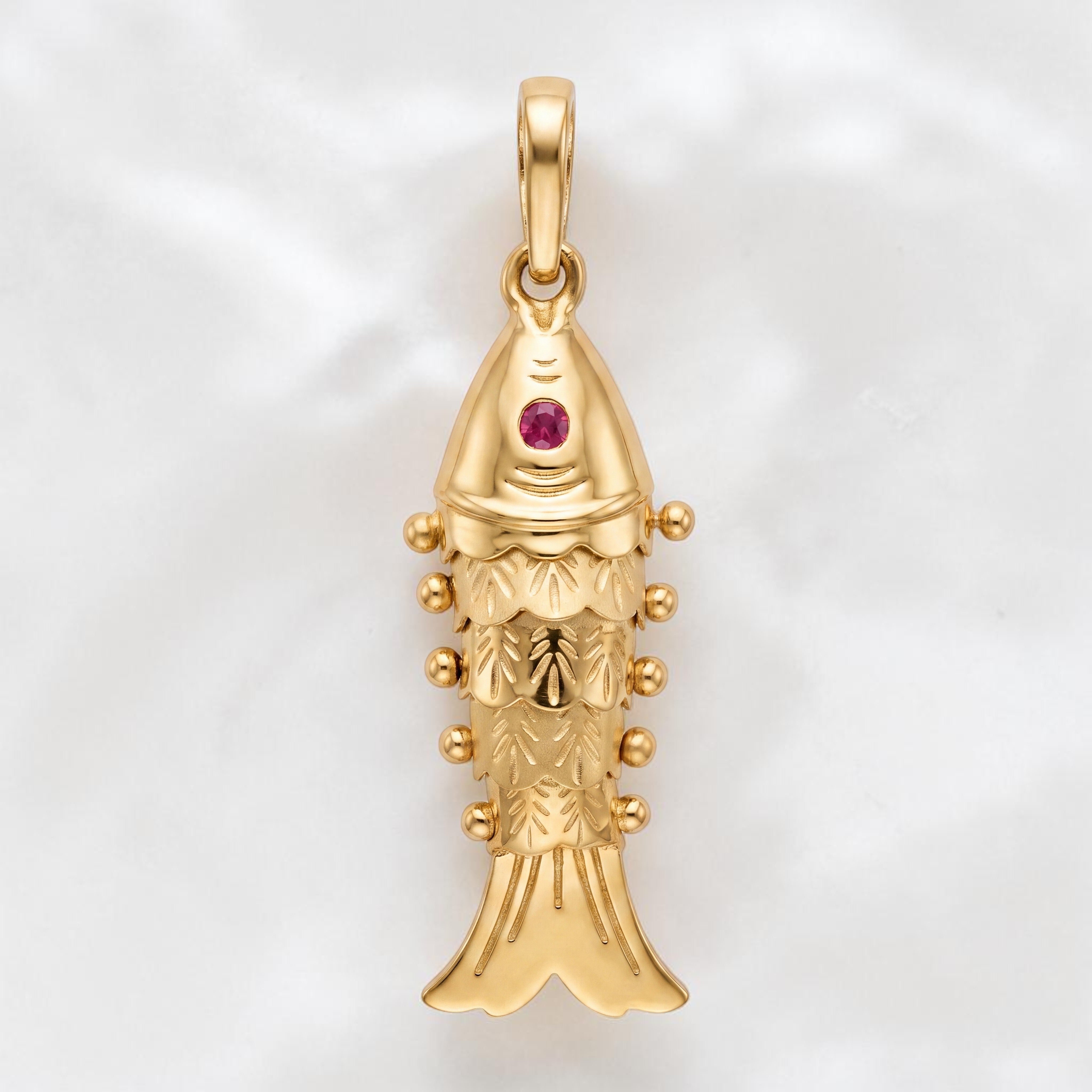 Yellow gold fish-shaped pendant featuring intricate engraved detailing, decorative bead accents, and a small pink gemstone set near the top for a classic traditional look.